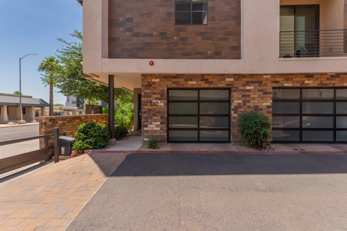This image showcases the property's modern facade with sleek glass garage doors and a landscaped front area. The exterior looks both upscale and welcoming, ideal for making a good first impression. Subtle activity cues, such as vehicles being parked and people gathering, imply ease of access and a vibrant yet professional atmosphere.