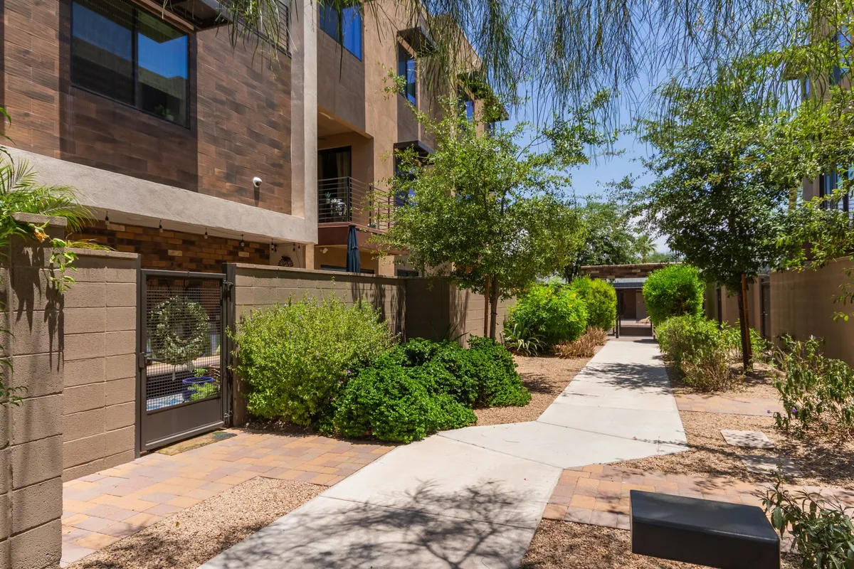 This image features a welcoming pathway surrounded by lush greenery and the building facade, inviting residents and guests to stroll through a tranquil setting. The scene is bright and open, emphasizing the connection between the home and the surrounding Old Town Scottsdale neighborhood.