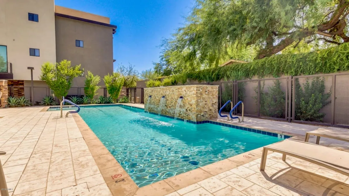 A tranquil swimming pool surrounded by lush greenery, comfortable lounge chairs, and a calming water feature. The setting invites relaxation after a day of exploring, while also suggesting opportunities for socializing or family fun within the community.