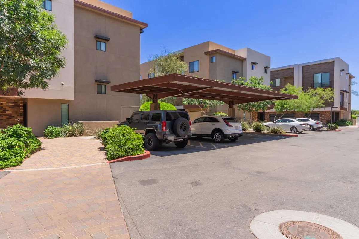 The photo features a covered parking area, modern architectural elements, and abundant greenery. It highlights the ease of parking and well-maintained outdoor spaces, suggesting convenience for travelers with vehicles and providing a snapshot of the building’s context within the city.