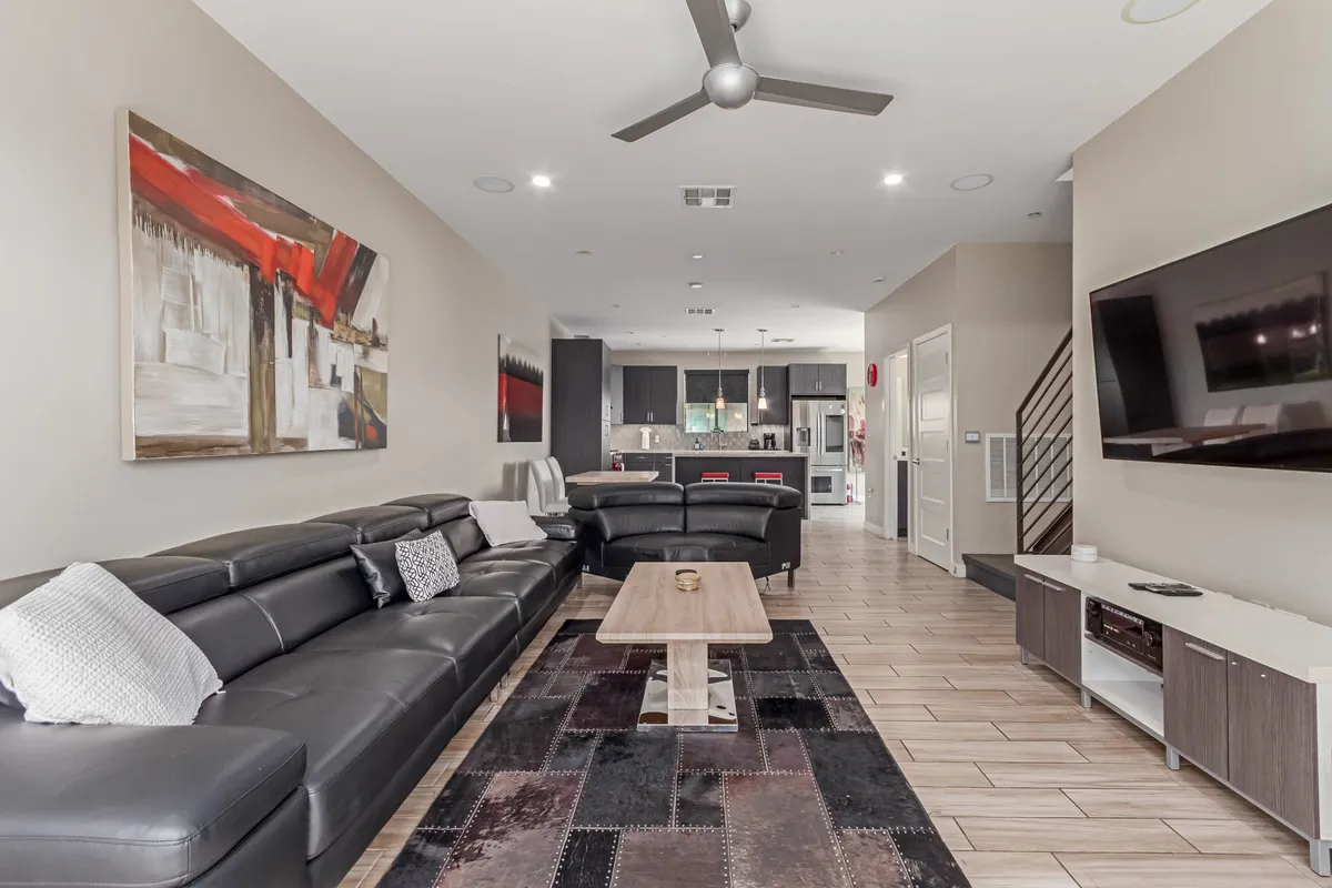 A wide-angle view of a large sectional sofa in a spacious living area, with a prominent art piece on the wall and the kitchen visible in the background. The space is bathed in natural light, enhancing the sense of openness and flow between social zones.