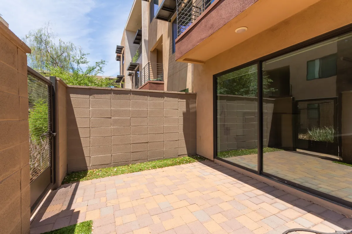 A paved patio flanked by surrounding walls and a glass door provides a tranquil spot for outdoor relaxation or dining. The space is bathed in natural light, suggesting an inviting transition between indoor and outdoor living.