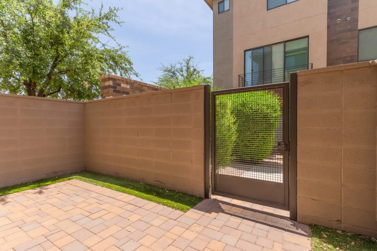 An exterior view featuring a gate, landscaped area, and the building’s facade, set in a welcoming atmosphere. The space hints at opportunities for morning solitude, social gatherings, or simply enjoying outdoor artful landscaping.