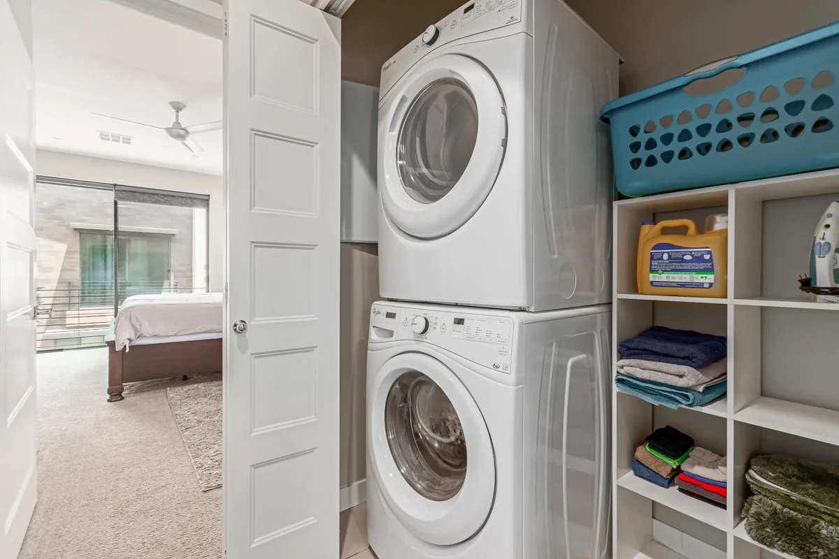 A compact yet highly organized laundry area with a stacked washer and dryer, neat shelving, and a laundry basket, all arranged for efficiency. The space is practical yet tidy, contributing to a clutter-free home.