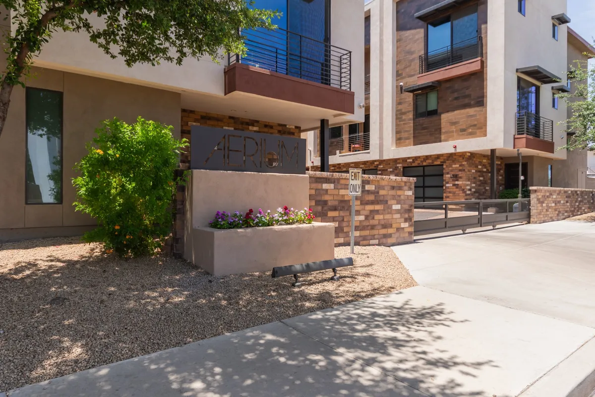 A view of the property’s modern exterior architecture, surrounded by thoughtful landscaping and visible signage, suggesting a vibrant and welcoming community. People can be imagined arriving home or mingling with neighbors in a well-maintained outdoor space.