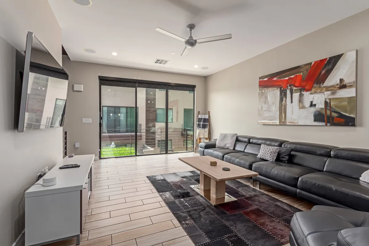 A contemporary living room with a leather sectional sofa, stylish coffee table, striking wall art, and sliding glass doors that let in abundant natural light. The layout encourages conversation and social gatherings, while the glass doors enhance the bright, airy ambiance.